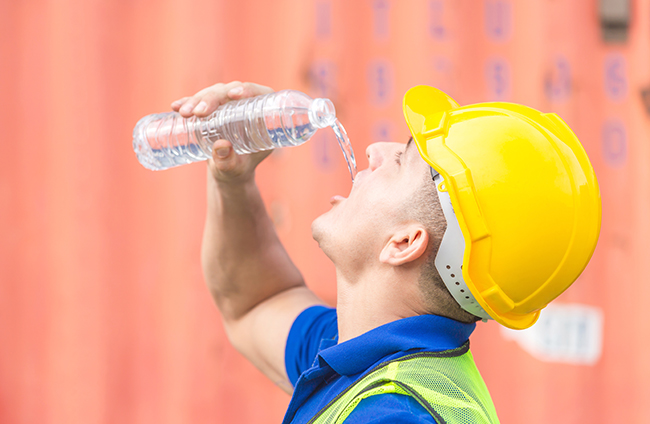 Close up of Worker man in hard hat drinking water at containers