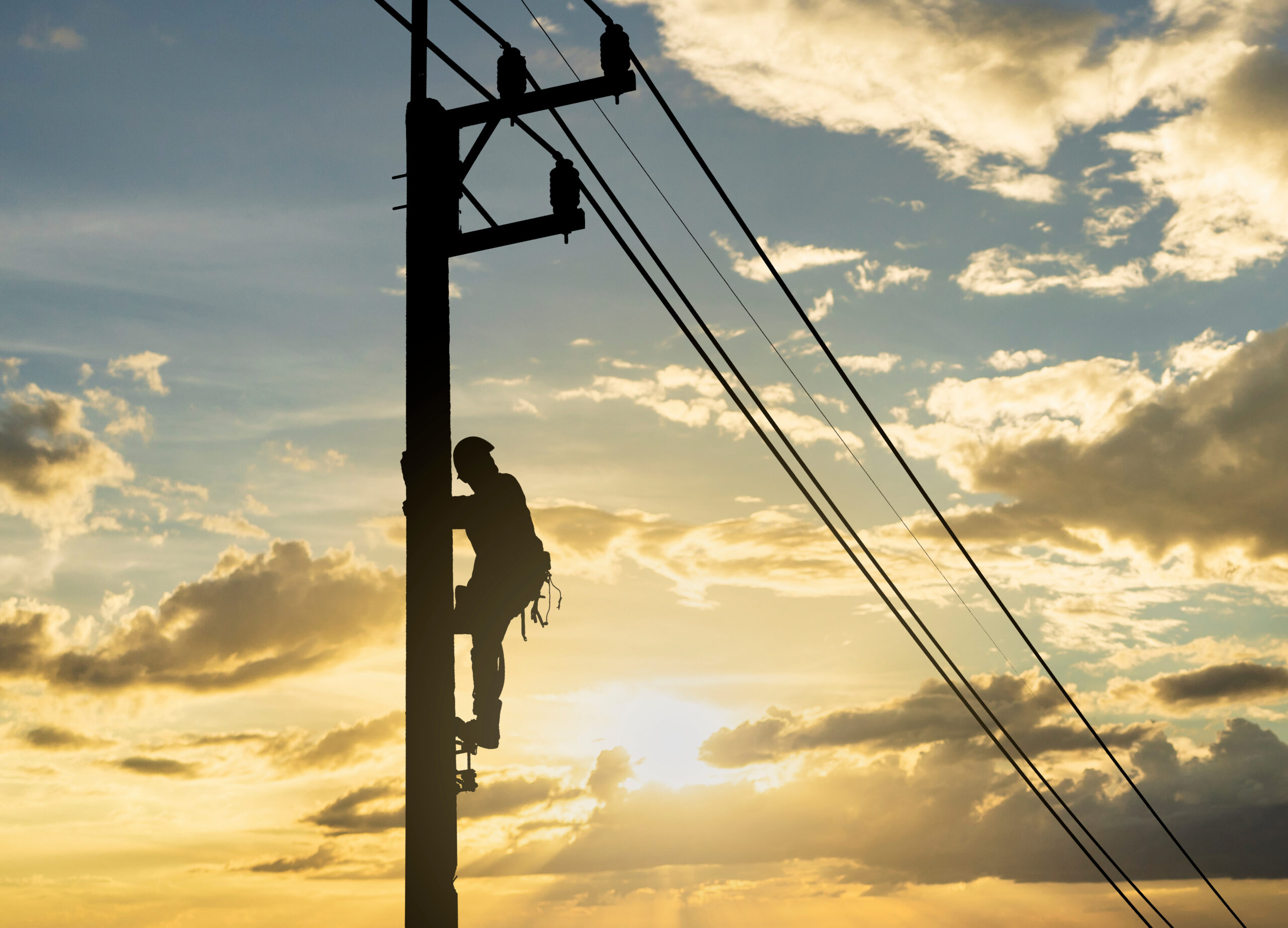 Silhouette man works with electricity on a pole with the sunset