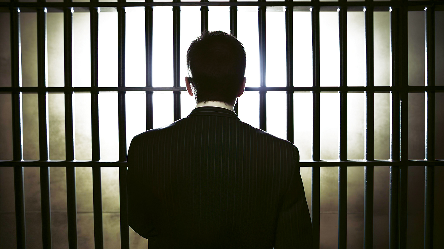 Close-up Of Businessman Hand Holding Metal Bars In Jail with dark environments.